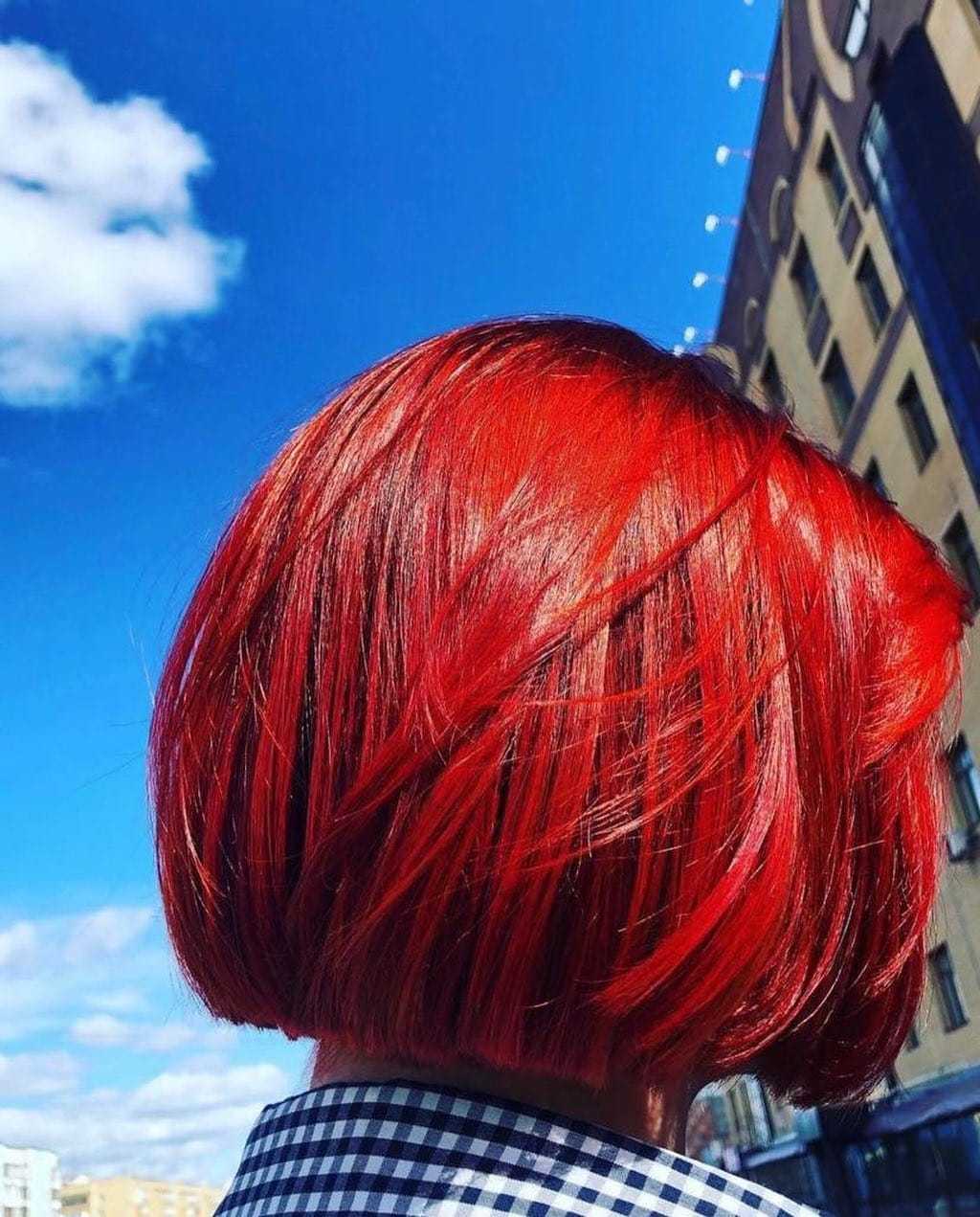 Vibrant red bob hairstyle against a bright blue sky backdrop.