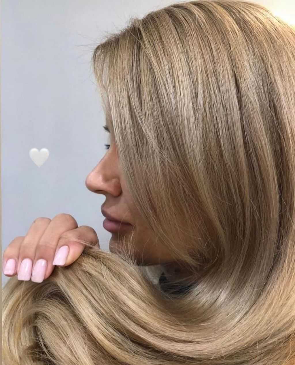 Woman with smooth blonde hair and manicured nails, holding hair gently in profile view.